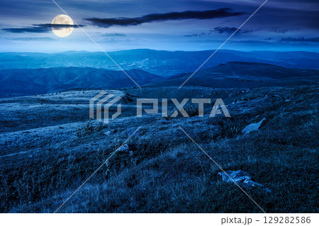 mountain landscape in summer at night. beautiful view of rolling green hills and alpine meadows in full moon light. scenery with clouds on the dark sky. scenic nature background for travel 129282586