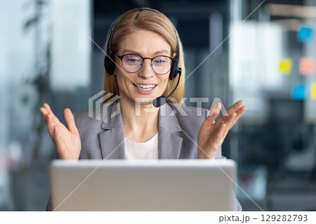 A businesswoman with a headset smiles during a video call, discussing a project in the office. 129282793