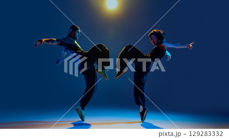 Urban dancers mid-air in mirrored kicks under spotlight with fierce emotional charge Urban dancers mid-air in mirrored kicks under spotlight with fierce emotional charge 129283332