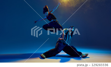 Female dancer mid-air in jump over male partner with explosive motion and focus 129283336