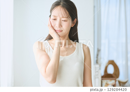 歯の痛みに苦しむ女性・頬を押さえるポーズ・白いタンクトップの若い女性 129284420