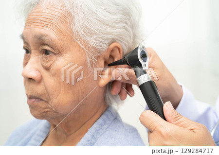 Otolaryngologist or ENT physician doctor examining senior patient ear with otoscope, hearing loss problem. 129284717