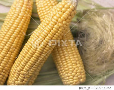 Fresh corn heads lie on corn leaves and corn silk on the table after cleaning, close up. Preparing corn for cooking. Natural food, healthy nutrition, yellow kernels, organic vegetable 129285062