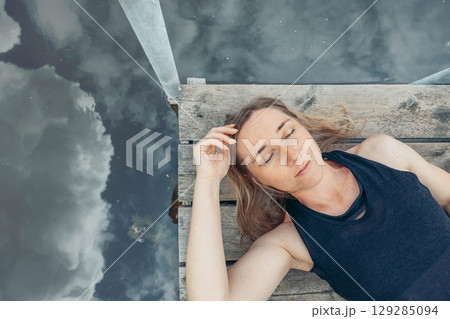 woman relaxing on dock surrounded by still water and green nature, concept of self care, weekend getaway, calm, top view woman relaxing on dock surrounded by still water and green nature, concept of self care, weekend getaway, calm, top view 129285094