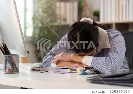 Office Syndrome: Exhausted young woman resting her head on paperwork at desk Office Syndrome: Exhausted young woman resting her head on paperwork at desk 129285196