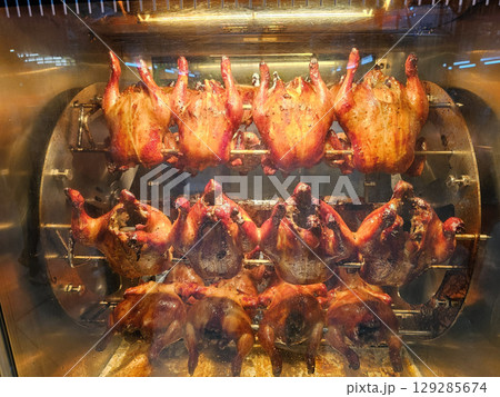Golden brown rotisserie chickens rotating on spits inside a commercial oven or display unit. Golden brown rotisserie chickens rotating on spits inside a commercial oven or display unit. 129285674
