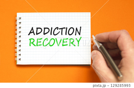 Addiction recovery symbol. Concept words Addiction recovery on beautiful white note. Psychologist hand. Beautiful orange table orange background. Psychology addiction recovery concept. Copy space. 129285993