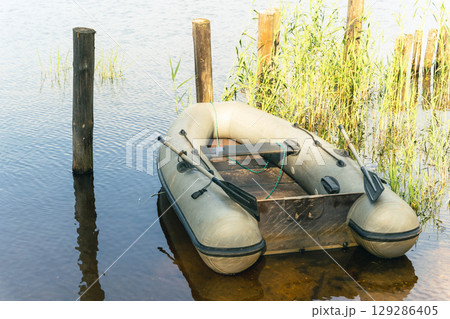 Inflatable boat moored near wooden pier on calm lake 129286405