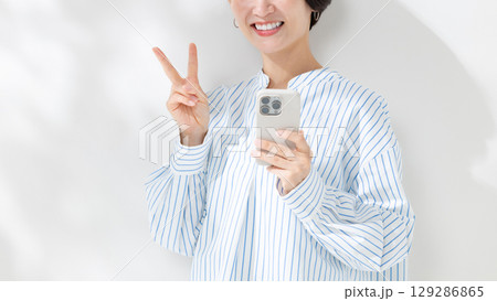 スマホを持ちピースサインをする女性 129286865