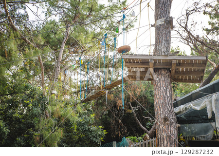 Side view full body of teenager in protective helmet riding on rope while entertaining in green jungle park 129287232