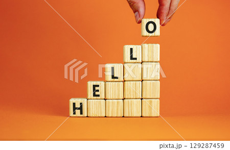 Hello symbol. Concept word Hello on beautiful wooden blocks. Beautiful orange table orange background. Businessman hand. Business lifestyle hello concept. Copy space. Hello symbol. Concept word Hello on beautiful wooden blocks. Beautiful orange table orange background. Businessman hand. Business lifestyle hello concept. Copy space. 129287459