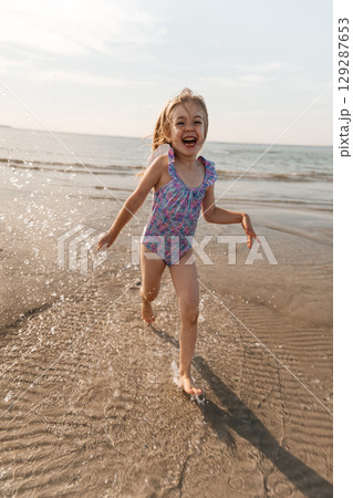 Child enjoys running in the surf on a sunny beach during golden hour Child enjoys running in the surf on a sunny beach during golden hour 129287653