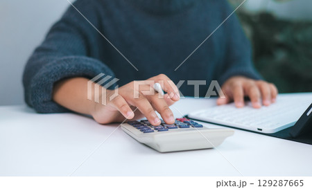 Person working on financial tasks with calculator and digital tablet, symbolizing accounting, budget management, tax preparation, and personal or small business financial services. Person working on financial tasks with calculator and digital tablet, symbolizing accounting, budget management, tax preparation, and personal or small business financial services. 129287665