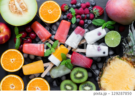 A colorful array of berry flavored ice cream pops sits atop a bed of fresh fruits, including kiwi, melon, and citrus. A colorful array of berry flavored ice cream pops sits atop a bed of fresh fruits, including kiwi, melon, and citrus. 129287850