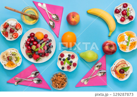 6 bowls of yogurt dressed with different ingredients fruit, berries, nuts, honey, and 6 spoons, napkins and right up some empty space on light blue background. Horizontal. Top view. 6 bowls of yogurt dressed with different ingredients fruit, berries, nuts, honey, and 6 spoons, napkins and right up some empty space on light blue background. Horizontal. Top view. 129287873