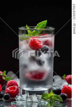 A glass of chilled mineral water with ice cubes and berries near spilled blueberries, strawberries and raspberries on a black background. Mineral water with berries. Vertical. A glass of chilled mineral water with ice cubes and berries near spilled blueberries, strawberries and raspberries on a black background. Mineral water with berries. Vertical. 129287937