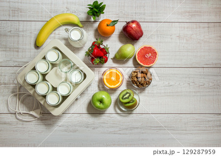 A vibrant collection of fruits including bananas, apples, and berries is placed on a wooden surface alongside a yogurt maker, promoting healthy eating and preparation. A vibrant collection of fruits including bananas, apples, and berries is placed on a wooden surface alongside a yogurt maker, promoting healthy eating and preparation. 129287959