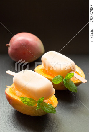 Mango sorbet ice cream on half cutted mango fruit behind mango on a black background. Mango fruit sorbet ice cream popsicles. Vertical. 129287987