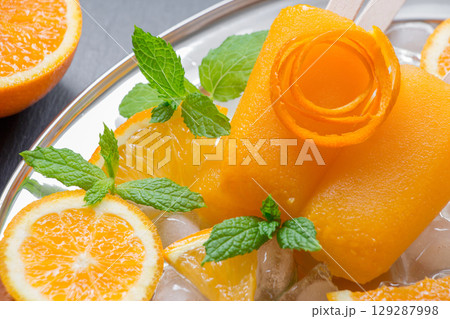 Bright orange ice cream is beautifully presented on a plate with refreshing orange slices and mint leaves, creating a perfect summer treat. Enjoying this dessert brings joy and freshness. Bright orange ice cream is beautifully presented on a plate with refreshing orange slices and mint leaves, creating a perfect summer treat. Enjoying this dessert brings joy and freshness. 129287998