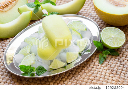 Lime melon ice cream popsicles presented on a silver tray surrounded by ice, mint, and lime, ideal for a warm afternoon gathering with friends or family. Lime melon ice cream popsicles presented on a silver tray surrounded by ice, mint, and lime, ideal for a warm afternoon gathering with friends or family. 129288004