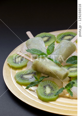 Kiwi sorbet ice cream popsicles on golden plate with ice cubes chopped kiwi slices and mint leaves on a black background. Kiwi sorbet ice cream popsicles. Vertical. Kiwi sorbet ice cream popsicles on golden plate with ice cubes chopped kiwi slices and mint leaves on a black background. Kiwi sorbet ice cream popsicles. Vertical. 129288018