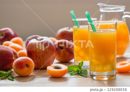 Refreshing juice made from apricots, apples, and peaches is served in tall glasses with green straws, surrounded by fresh fruits and mint leaves on a wooden table. Refreshing juice made from apricots, apples, and peaches is served in tall glasses with green straws, surrounded by fresh fruits and mint leaves on a wooden table. 129288038