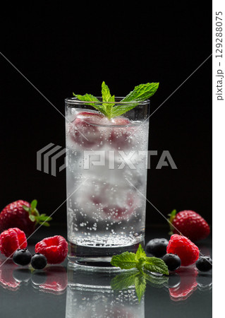 Iced water captures freshness with floating berries and mint, serving as the perfect drink for relaxation. The bright colors contrast beautifully against the dark backdrop. 129288075