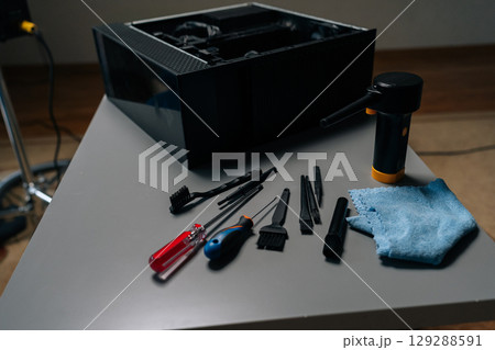 Cleaning open computer case with specialized tools like screwdrivers and brushes on gray table in workshop, ensuring optimal performance and preventing overheating, close-up, no people. 129288591