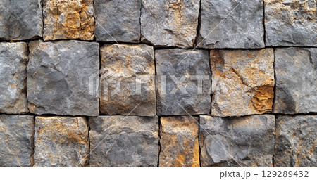 A close-up view of a stone wall made of variously shaped and colored stones, showcasing a rustic and textured appearance. 129289432