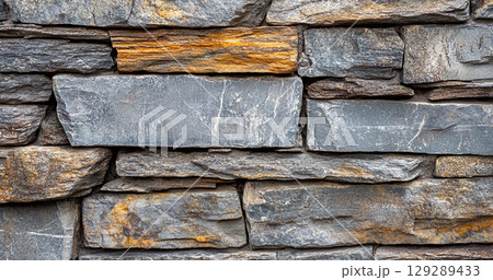 A close-up view of a stone wall made of variously shaped and colored stones, showcasing a rustic and textured appearance. 129289433