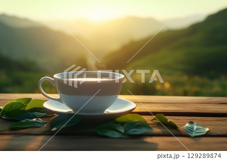 A close-up view of a white cup filled with black tea sits on a rustic wooden table surrounded by green tea petals glowing softly in golden sunlight 129289874
