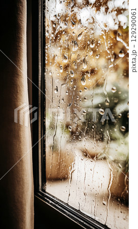 Raindrops trickle down a glass window, blurring the vibrant autumn leaves outside. The scene evokes a cozy atmosphere perfect for enjoying a quiet afternoon indoors 129290061
