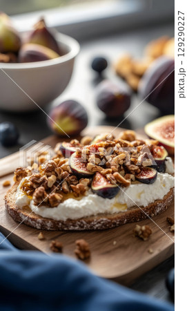 Freshly prepared toasts feature creamy cheese topped with sliced figs and chopped nuts, creating an appetizing dish on a rustic wooden table illuminated by soft sunlight 129290227