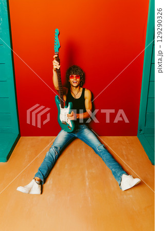 A man is holding a guitar and is sitting on the floor 129290326