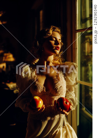 A woman is holding two apples in her hands while standing in front of a window 129290340