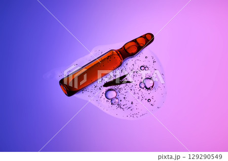 An ampoule with serum in its texture on a purple background with a leaf. 129290549