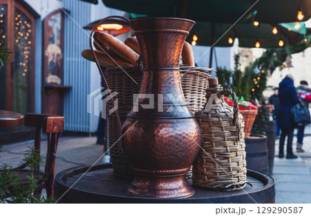 Vintage copper jug, braided wine bottle and french baguette in wicker basket on wooden barrel 129290587