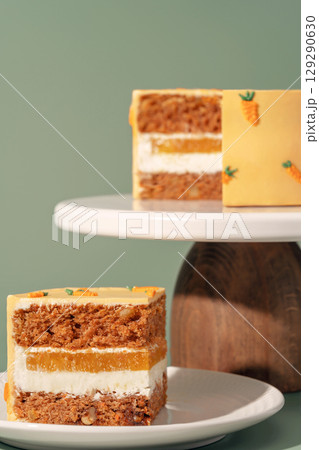 Bento cake featuring layers of carrot, orange, and mango, beautifully presented on a white cake stand against a soft green background, showcasing vibrant colors and textures for dessert lovers Bento cake featuring layers of carrot, orange, and mango, beautifully presented on a white cake stand against a soft green background, showcasing vibrant colors and textures for dessert lovers 129290630