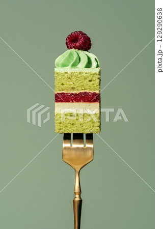 Layered bento cake featuring vibrant raspberry and pistachio sponge, topped with creamy frosting and a fresh raspberry, elegantly presented on a golden fork against a soft green background Layered bento cake featuring vibrant raspberry and pistachio sponge, topped with creamy frosting and a fresh raspberry, elegantly presented on a golden fork against a soft green background 129290638