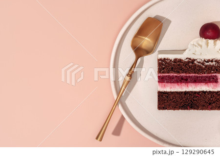 Bento cake with layers of chocolate and cherry, topped with whipped cream and a cherry, served on a white plate with a golden spoon, creating a delightful dessert experience Bento cake with layers of chocolate and cherry, topped with whipped cream and a cherry, served on a white plate with a golden spoon, creating a delightful dessert experience 129290645