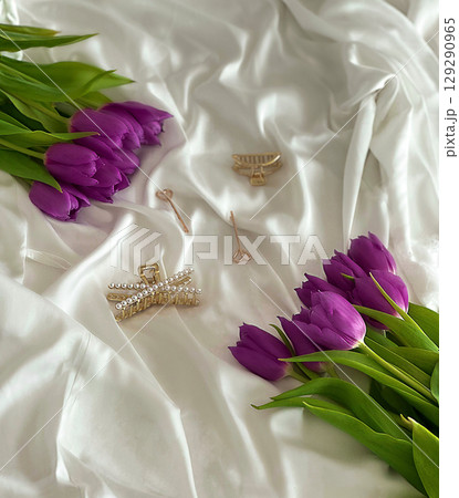 Purple tulips arranged on white satin fabric with elegant jewelry pieces, showcasing beauty and lifestyle themes. 129290965