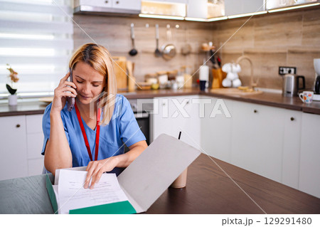 Female Doctor Working From Home and Consulting Patients by Phone 129291480