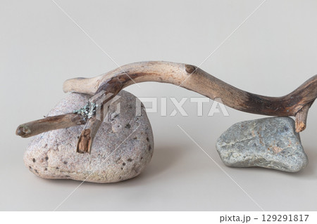 A dry tree branch and stones on a light background. Minimalistic creative composite background for the presentation of cosmetics or products. Front view 129291817