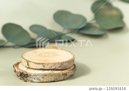 A round wooden pedestal on a light background and a branch of eucalyptus. A place for advertising. A round wooden pedestal on a light background and a branch of eucalyptus. A place for advertising. 129291818