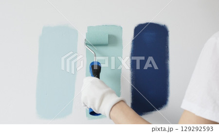 Painter wearing protective gloves rolling blue paint on white wall, creating gradient color effect for home interior renovation project Painter wearing protective gloves rolling blue paint on white wall, creating gradient color effect for home interior renovation project 129292593
