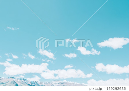 Bright blue sky with fluffy clouds over majestic mountains under midday light Bright blue sky with fluffy clouds over majestic mountains under midday light 129292686