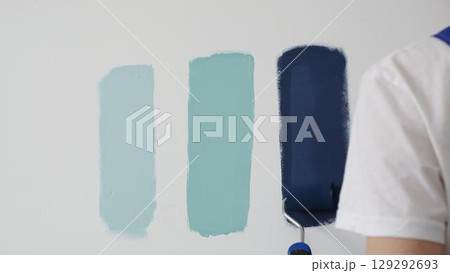 Painter wearing protective gloves rolling blue paint on white wall, creating gradient color effect for home interior renovation project 129292693