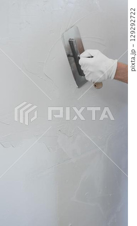 Professional construction worker is using a finishing trowel to carefully apply plaster on a wall, demonstrating expertise in home renovation and interior finishing, close-up of hand 129292722