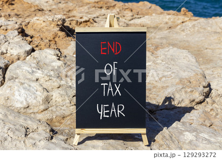 End of tax year symbol. Concept words phrase End of tax year on beautiful black blackboard. Beautiful stone blue sea sky background. Business End of tax year concept. Copy space. 129293272