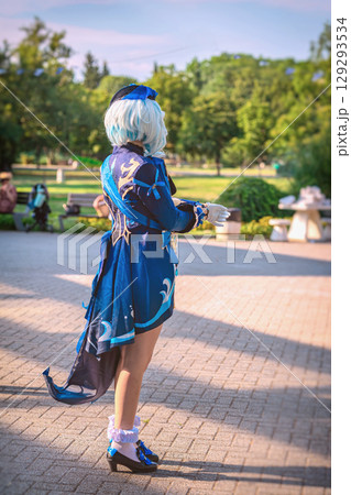 Cosplayer woman in detailed blue anime costume with wig and gloves standing outdoors in sunny park. Concept of cosplay character, anime costume, fan culture Cosplayer woman in detailed blue anime costume with wig and gloves standing outdoors in sunny park. Concept of cosplay character, anime costume, fan culture 129293534